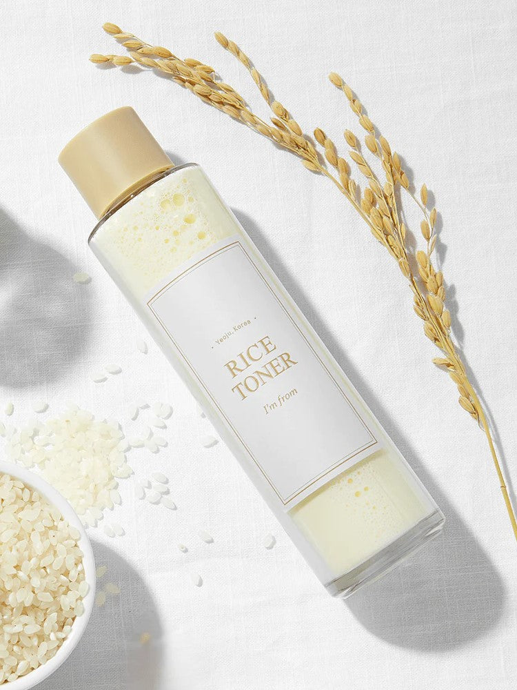 A bottle of 'I'm From' Rice Toner on a white background, surrounded by rice grains and a rice stalk.