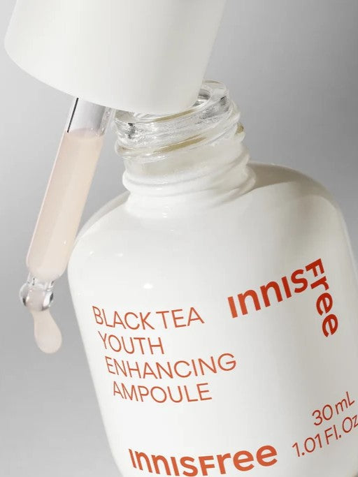 A close-up of Innisfree's Black Tea Youth Enhancing Ampoule with a dropper dispensing a pale liquid, highlighting its sleek white bottle design and rejuvenating formula.
