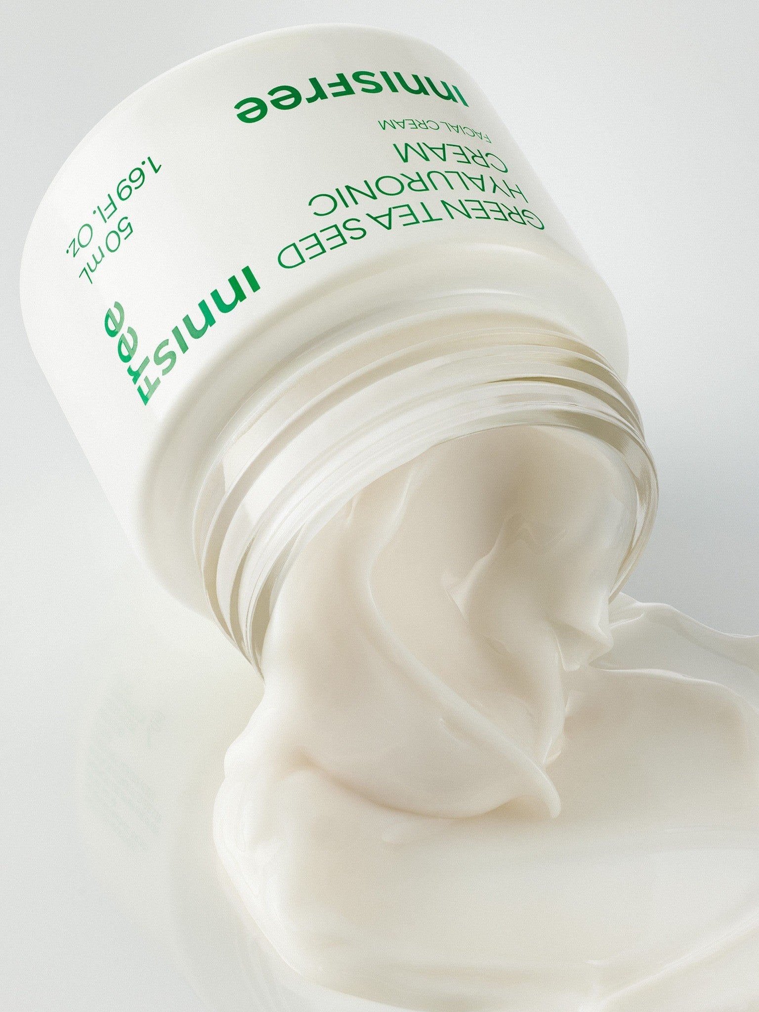 A jar of Innisfree Green Tea Seed Hyaluronic Cream spilling its creamy texture, showcasing its rich and nourishing consistency.