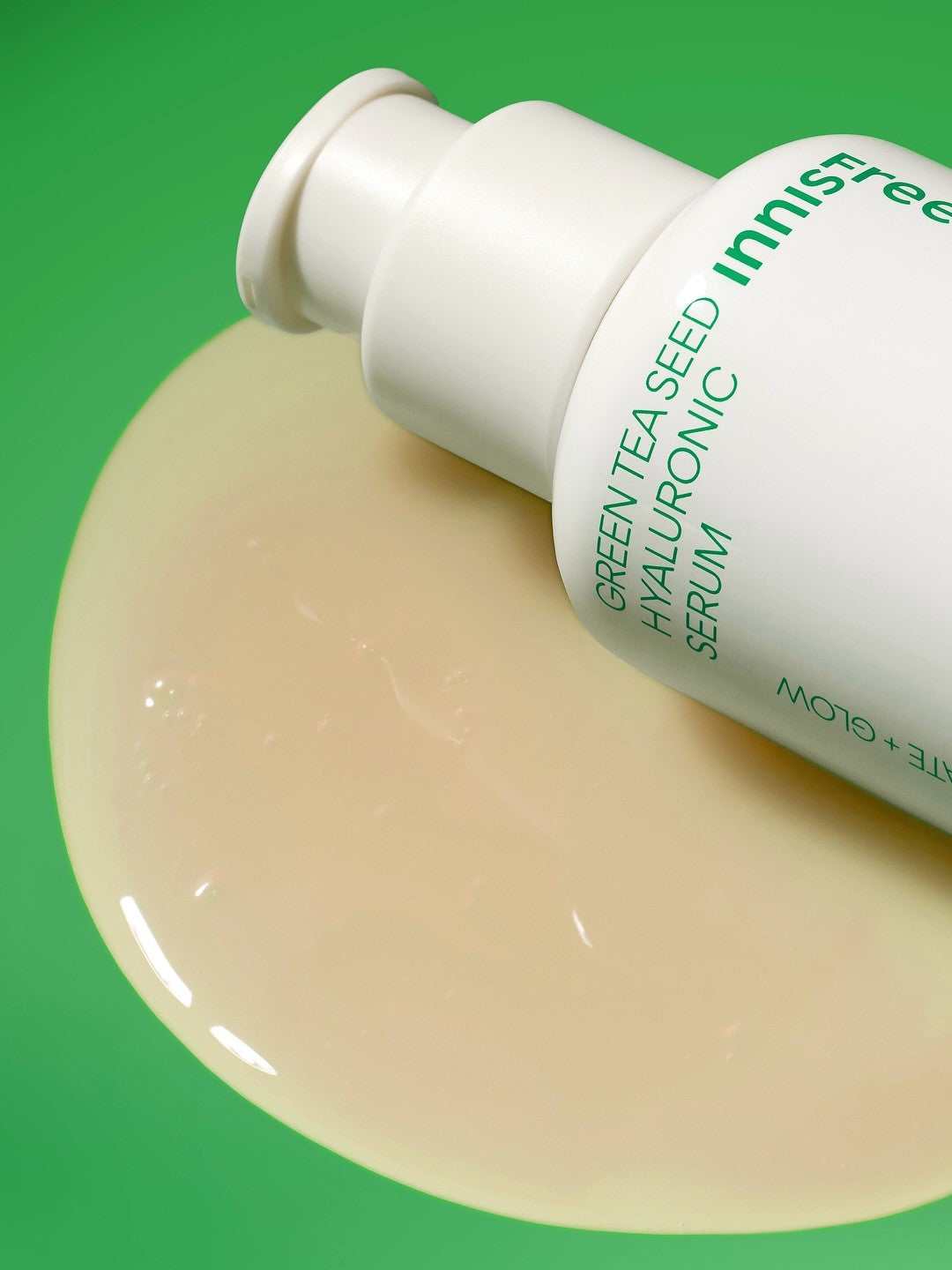 Close-up of Innisfree Green Tea Seed Hyaluronic Serum bottle with its glossy texture drop on a vibrant green background, highlighting its hydrating formula.