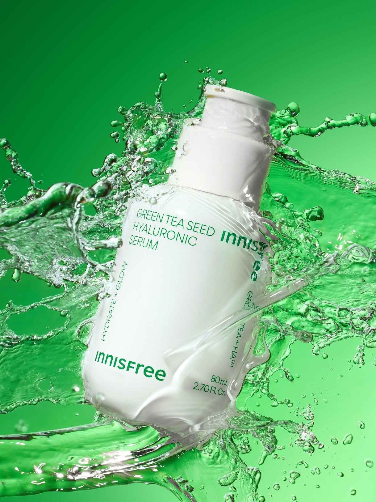 White bottle of Innisfree Green Tea Seed Hyaluronic Serum surrounded by splashes of water against a vibrant green background, emphasizing hydration and freshness.
