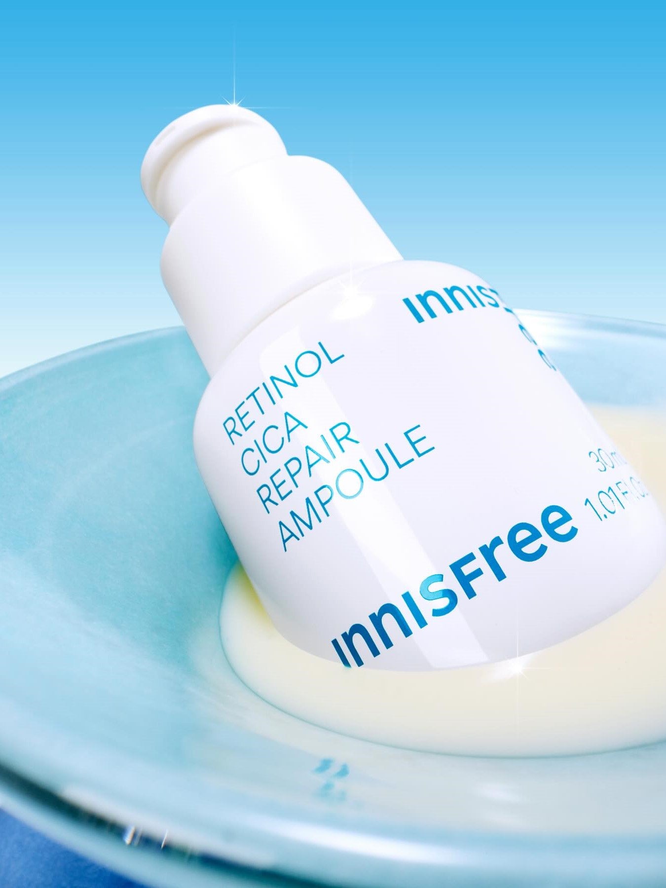 Close-up of Innisfree Retinol Cica Repair Ampoule bottle resting in a pale blue dish, showcasing its smooth texture against a bright background.