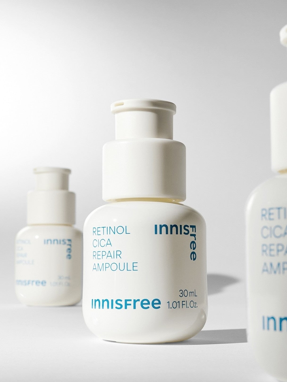 Three white bottles of Innisfree's Retinol Cica Repair Ampoule, each labeled with blue text, on a minimalist backdrop.