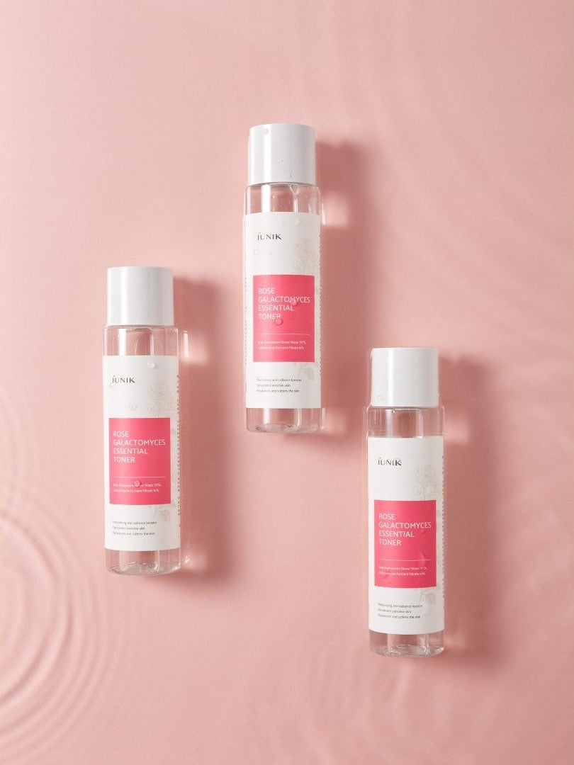 Three bottles of iUNIK Rose Galactomyces Essential Toner on a pink background, highlighting product branding and skincare benefits.