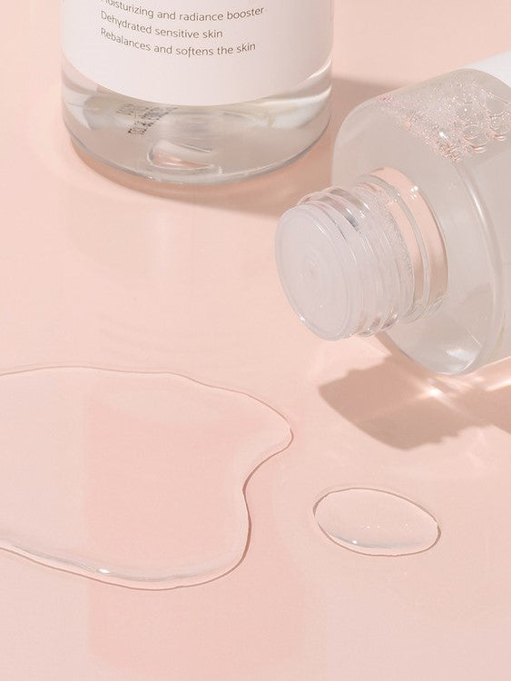 Close-up of iUNIK Rose Galactomyces Essential Toner’s clear, lightweight texture with fluid droplets on a soft pink surface, highlighting its hydrating and soothing properties.