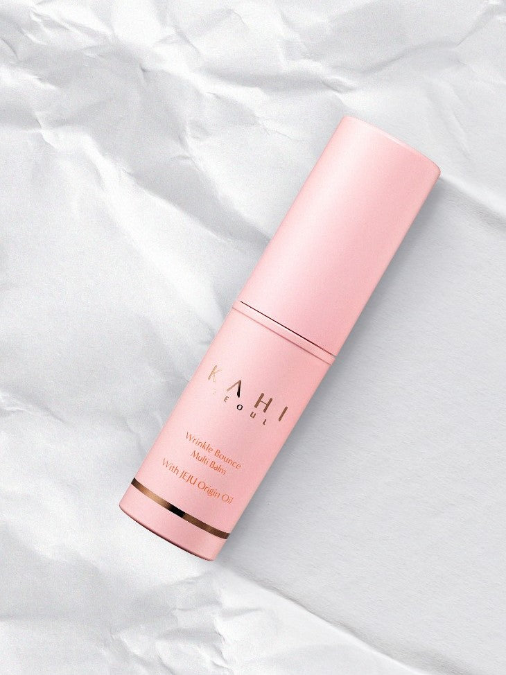 A pink cylinder container of Kahi Wrinkle Bounce Multi Balm with Jeju Origin Oil, placed on a crumpled white paper background.
