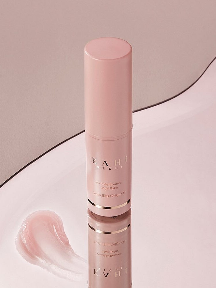A pink Kahi Wrinkle Bounce Multi Balm bottle reflecting on a smooth surface, accompanied by a creamy swatch of the balm.