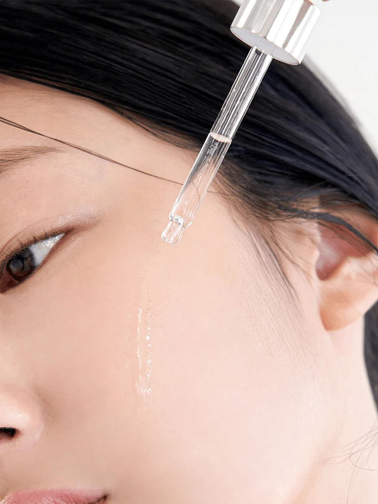 Close-up of a dropper dispensing Klairs Freshly Juiced Vitamin Drop onto a model's cheek, highlighting the serum's lightweight texture and brightening benefits.