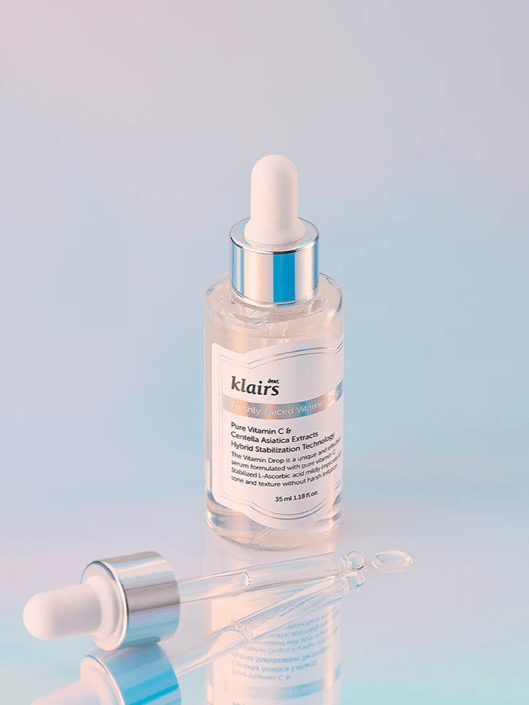 Klairs Freshly Juiced Vitamin Drop in a transparent serum bottle with a dropper, set against a soft pastel gradient background, emphasizing its brightening formula.