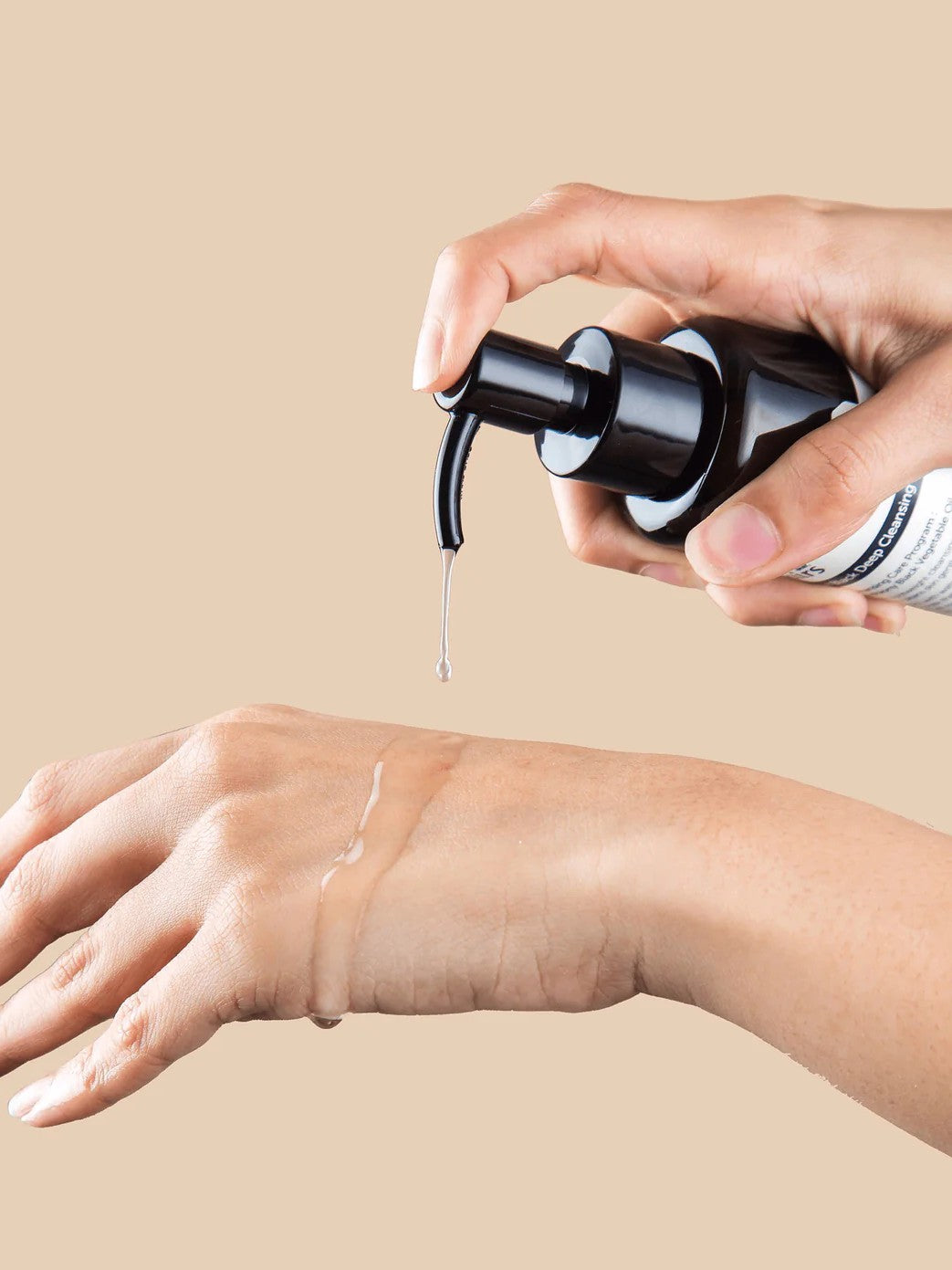 Hand applying a pump of Klairs Gentle Black Deep Cleansing Oil to another hand, showcasing its smooth texture against a beige background.