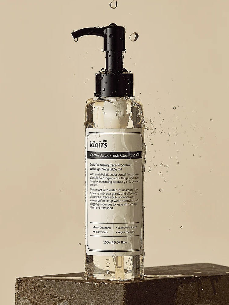 Klairs Gentle Black Fresh Cleansing Oil in a sleek bottle with a pump, surrounded by glistening water droplets on a textured surface.