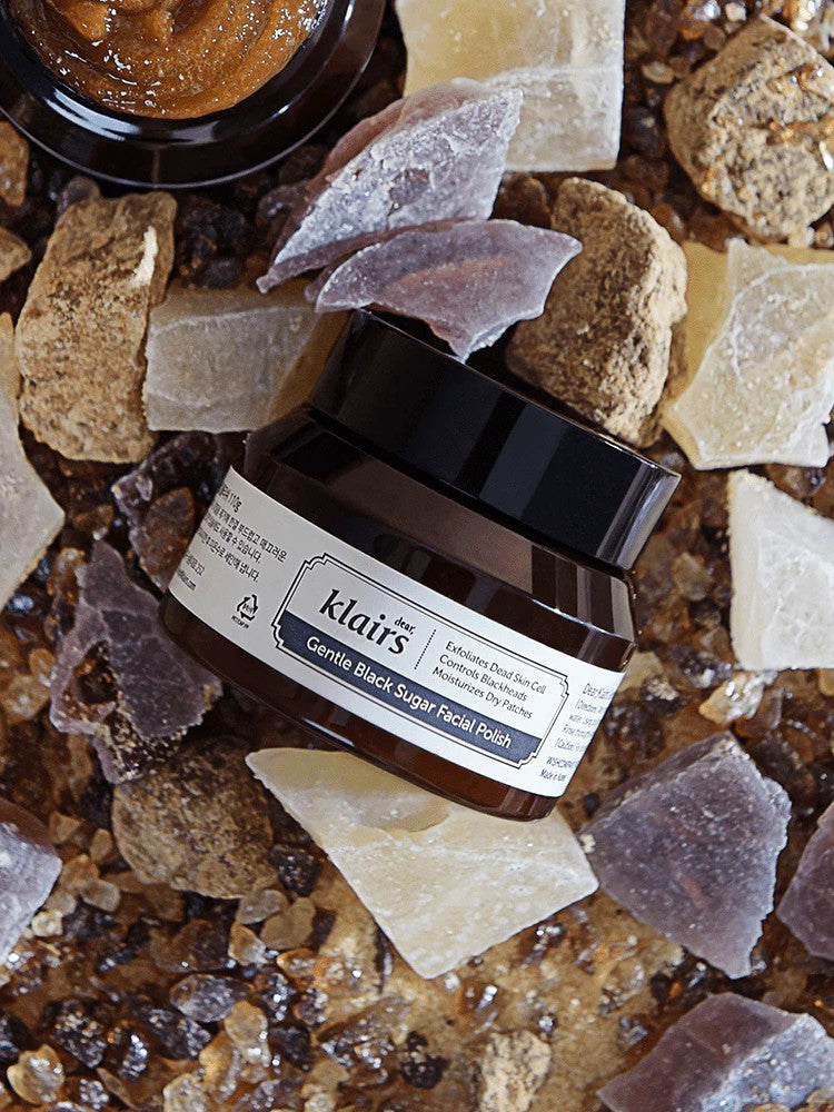 Klairs Gentle Black Sugar Facial Polish in a sleek jar surrounded by natural textured stones and sugar crystals on a rustic surface, highlighting its exfoliating properties.