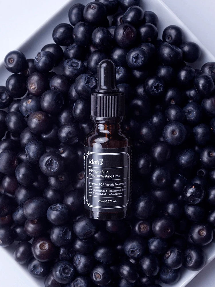 Klairs Midnight Blue Youth Activating Drop bottle placed on a bed of fresh blueberries, highlighting its antioxidant-rich formula and natural ingredients.