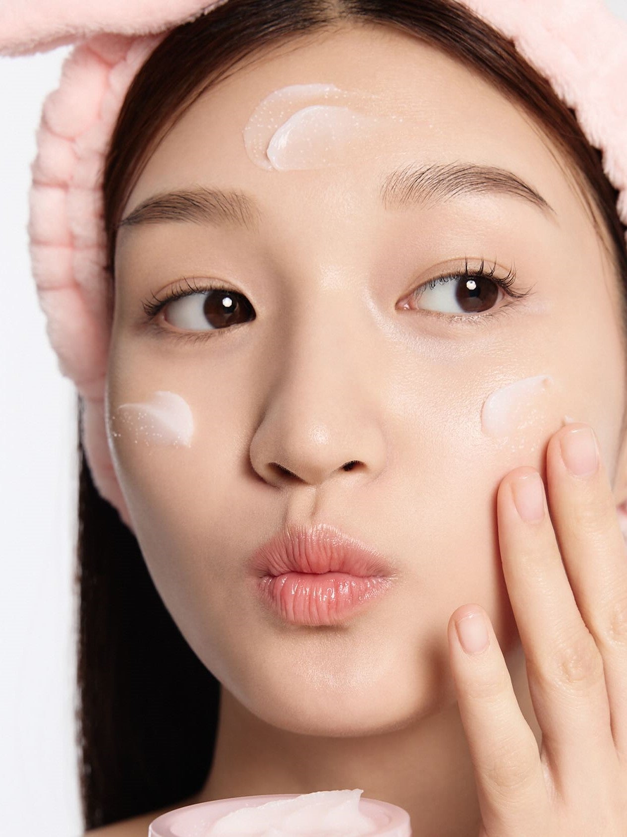 A model with long hair and a fluffy pink headband applies Laneige Bouncy & Firm Sleeping Mask, showcasing its creamy texture.