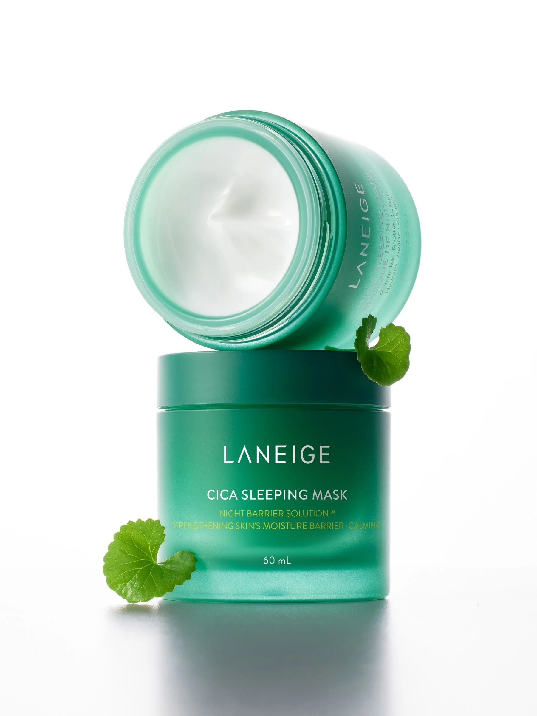 A green jar of Laneige Cica Sleeping Mask opened to reveal creamy texture, with a Centella Asiatica leaf beside it on a white background, highlighting its key ingredient.