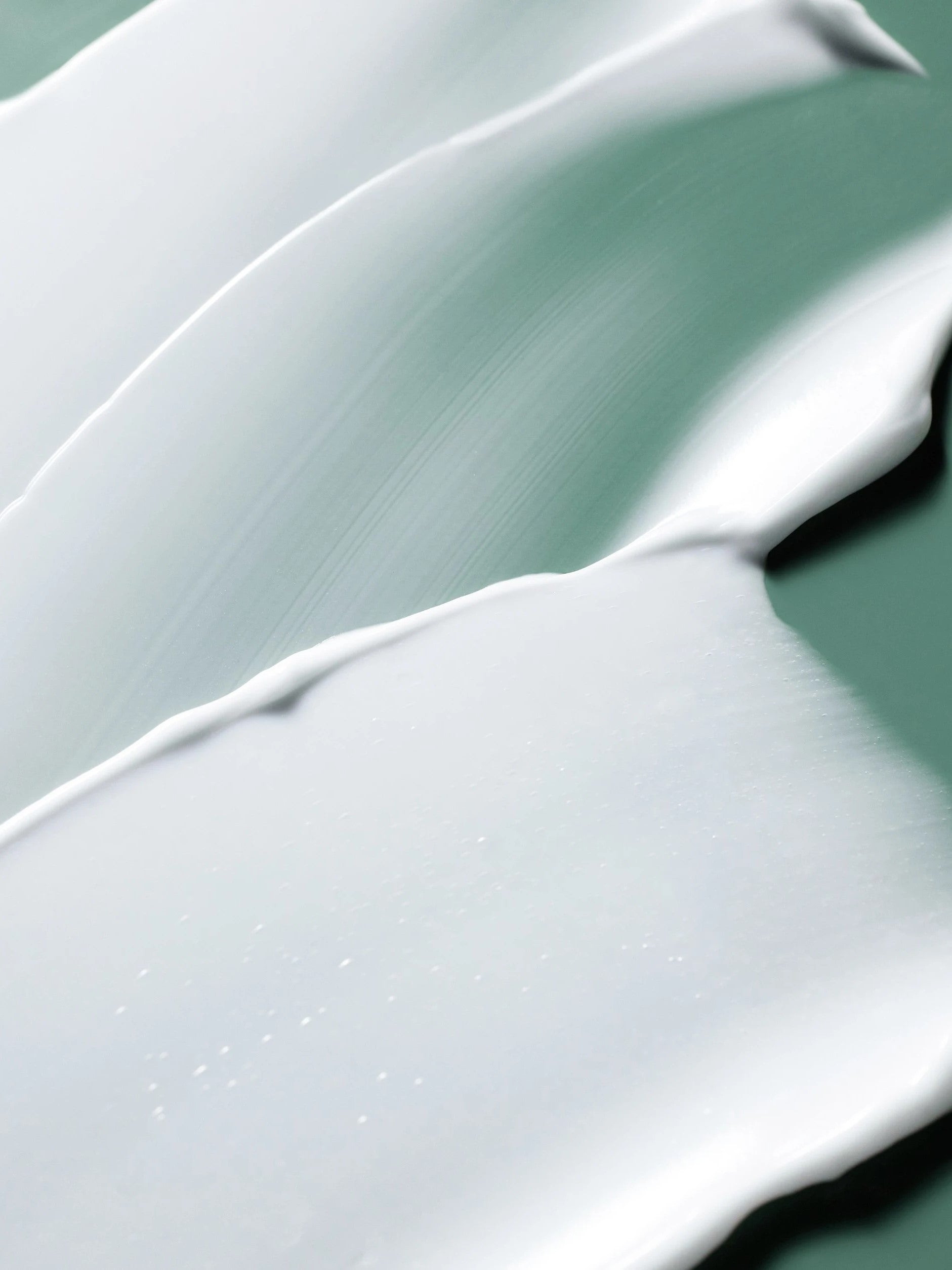 Close-up of smooth, creamy white samples of the Laneige Cica Sleeping Mask on a soft green backdrop.