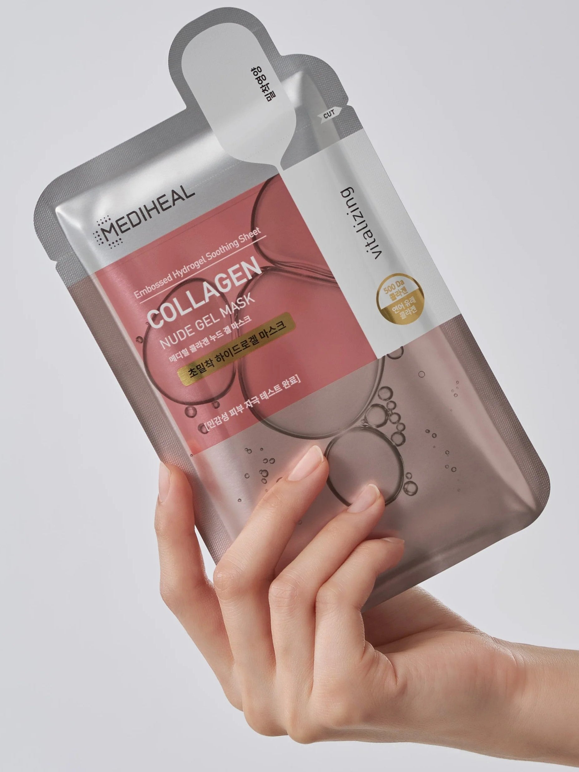 A hand holding a Mediheal Collagen Nude Gel Mask, showcasing sleek silver packaging with pink and bubble accents.