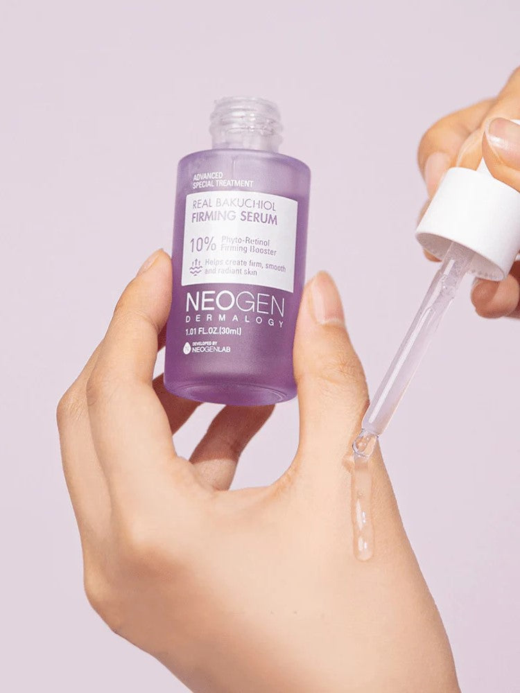 A hand holding a purple bottle of Neogen Dermalogy Real Bakuchiol Firming Serum with a dropper dispensing liquid serum, highlighting its firming and anti-aging properties.