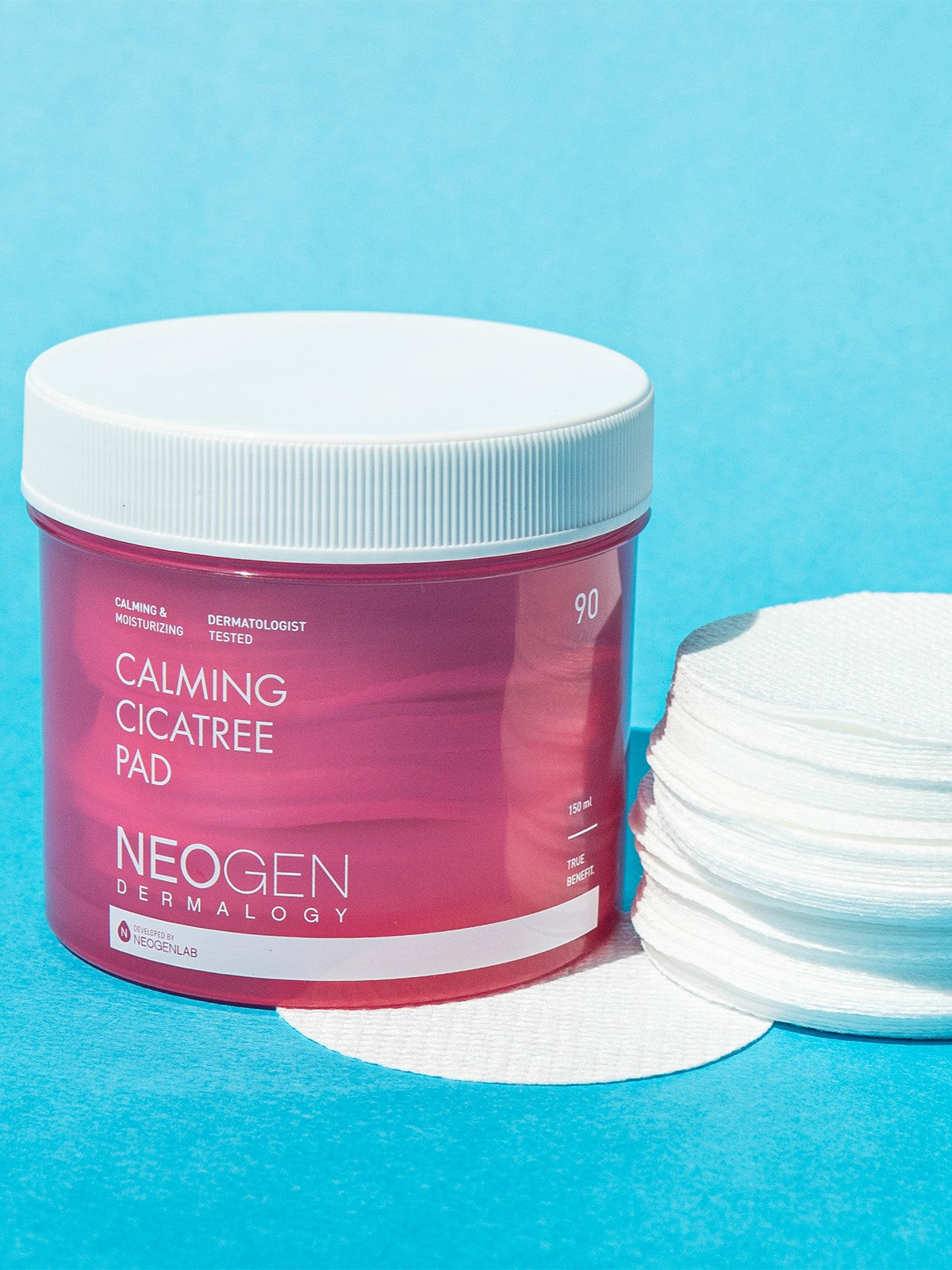 Neogen Dermalogy Calming Cica Tree Pads in a pink jar with a white lid, arranged next to stacked cotton pads on a bright blue background, highlighting their calming and soothing skincare benefits.