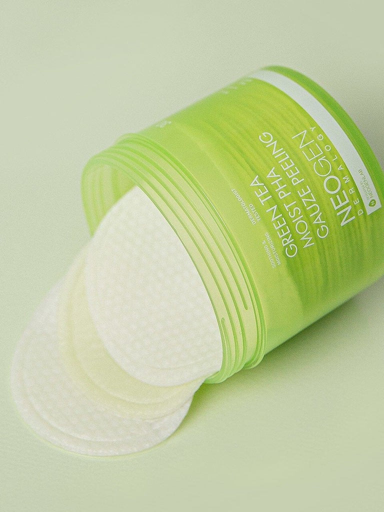 Green container of Neogen's Green Tea Moist PHA Gauze Peeling Pads with partially visible pads, set against a light green background, highlighting their exfoliating and moisturizing benefits.