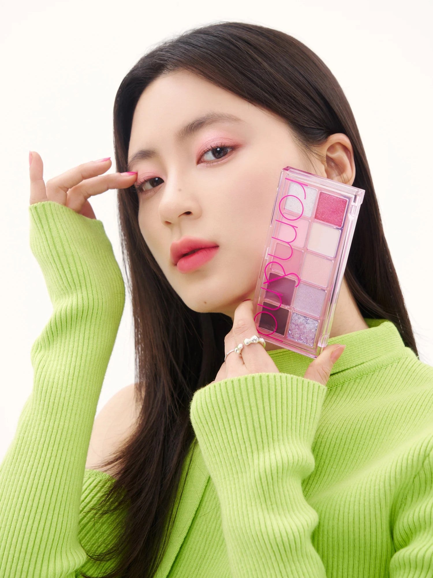 A model in a bright green sweater holds the Romand Better Than Palette Energetic Series in Berry Fuchsia Garden, showcasing the eyeshadow applied on her eyes.