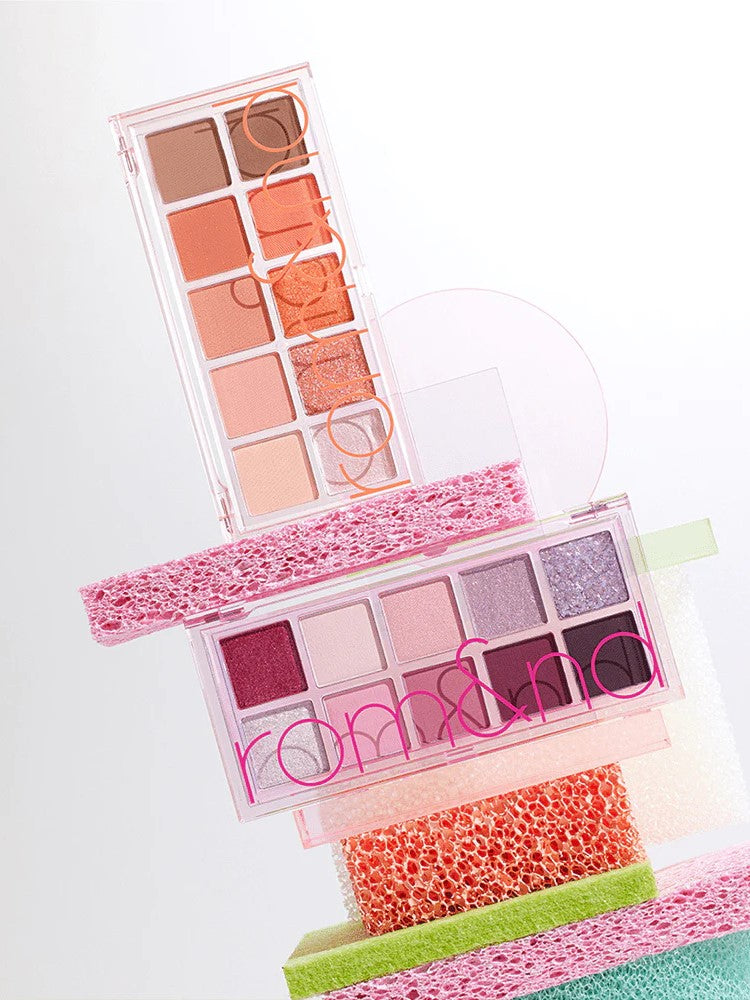 Two Romand Better Than Palette Energetic Series eyeshadow palettes stacked on vibrant sponges, showcasing shades from warm neutrals to rich purples.