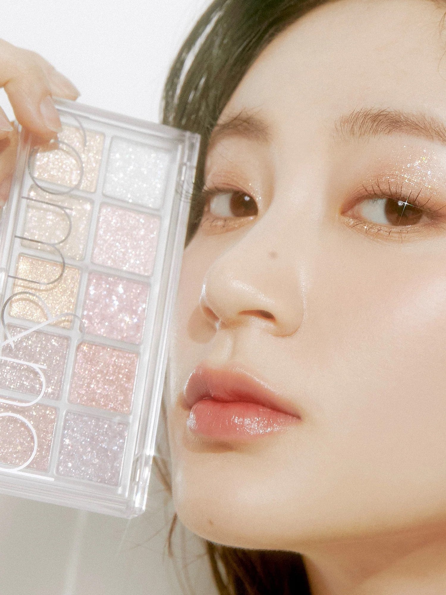 A model holds the glittery Romand Better Than Palette Light and Glitter Garden eyeshadow palette, showing the shimmering shades applied on her eyes.