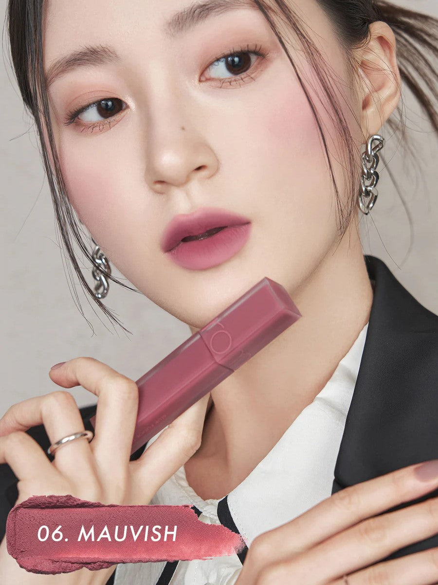 A model wearing Romand Blur Fudge Tint in the shade Mauvish, showcasing the soft matte texture on her lips.