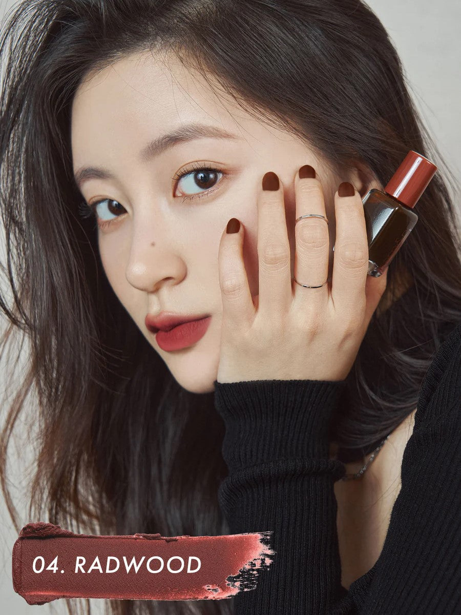 A model wearing Romand Blur Fudge Tint in the shade Radwood, showcasing the soft matte texture on her lips.