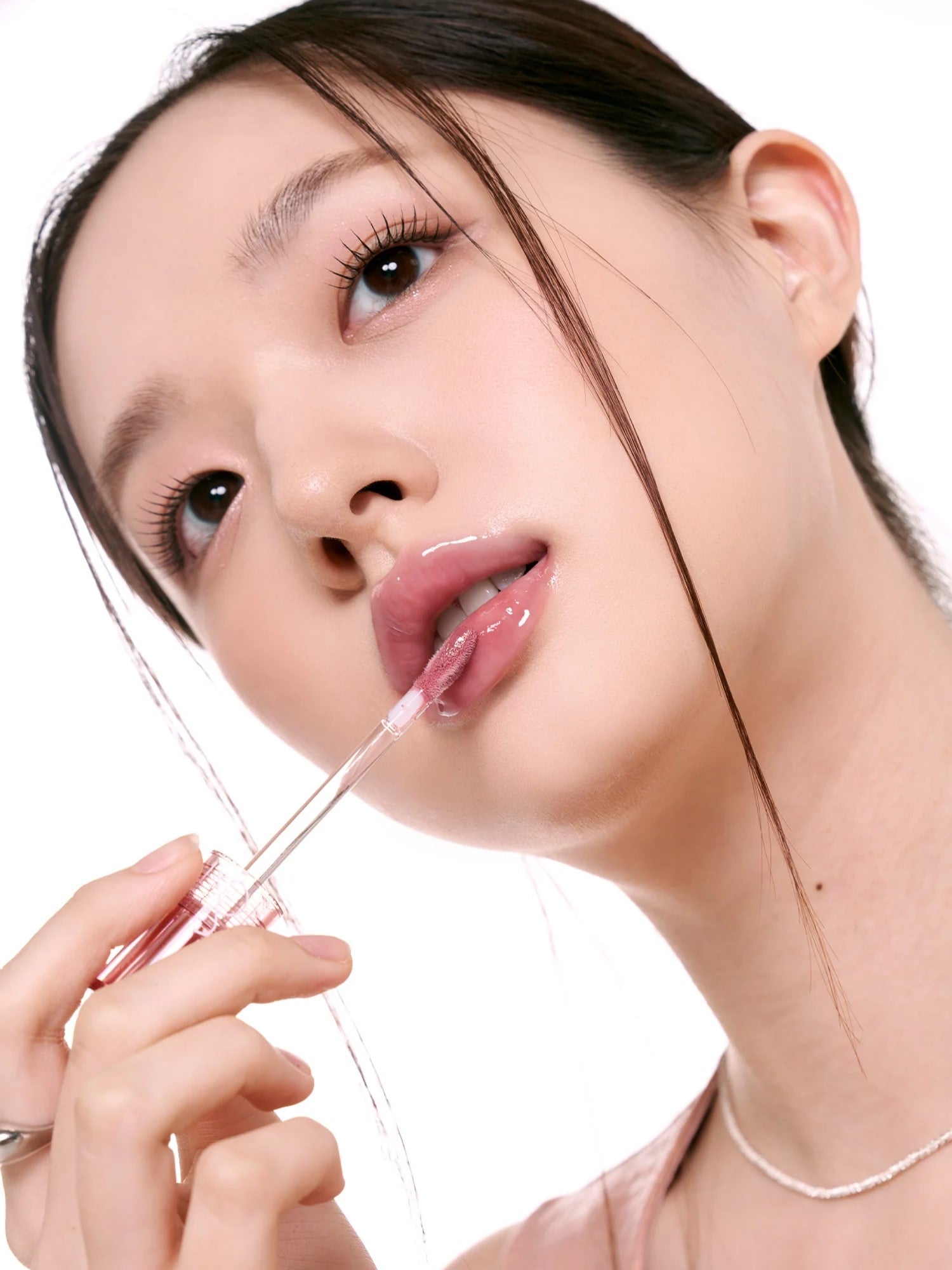 A model with sleek hair holds the Romand Glasting Color Tint, highlighting its plumping and high-shine glossy finish.