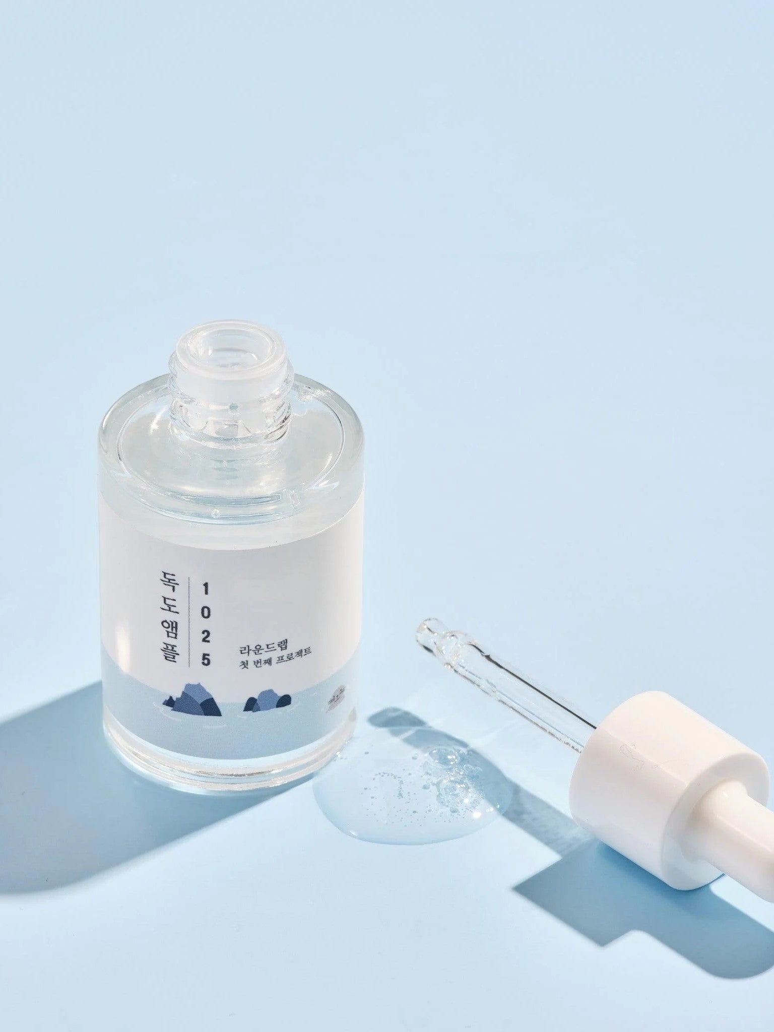 Round Lab 1025 Dokdo Ampoule with dropper and droplet, set against a light blue background.