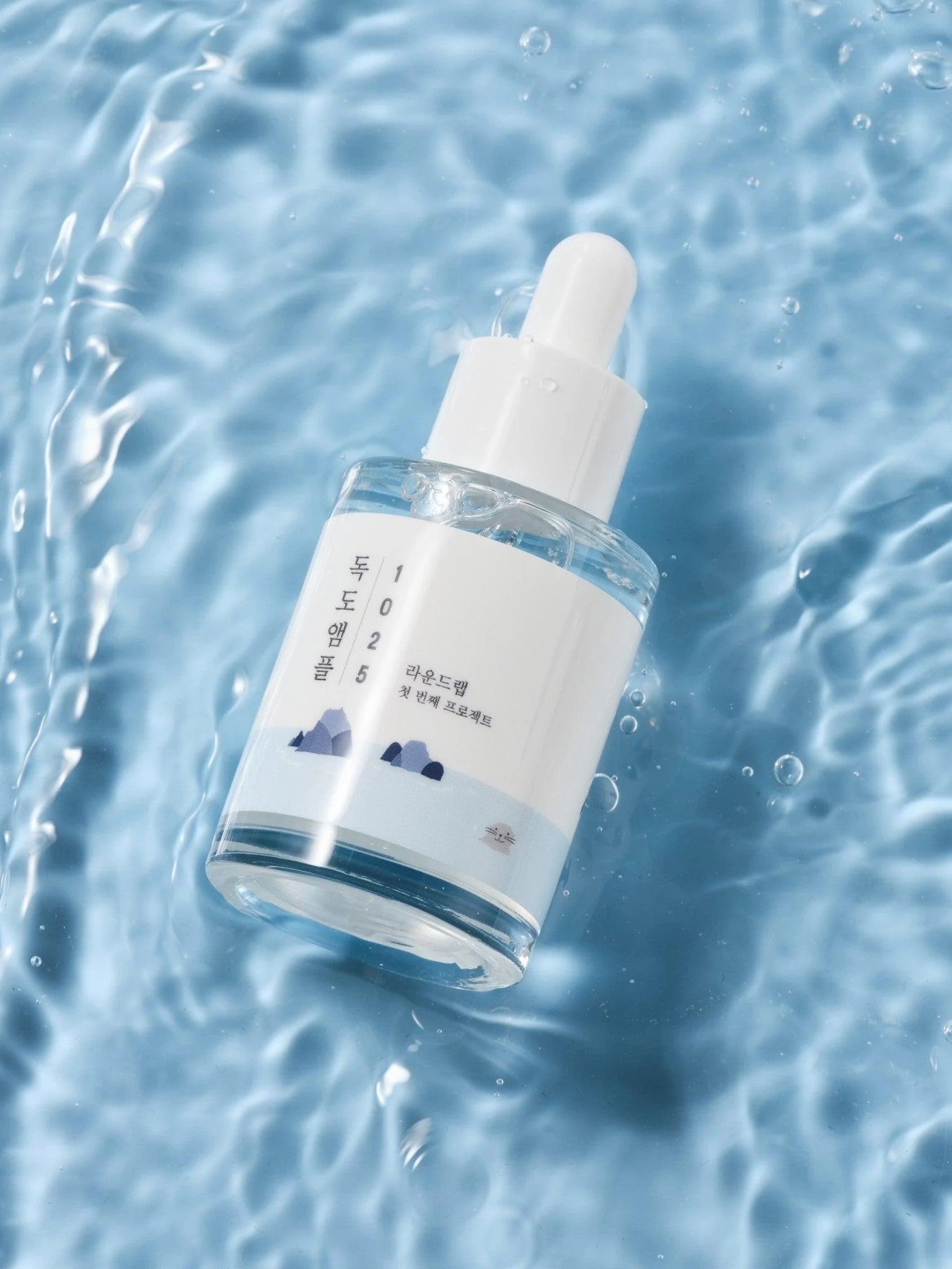 Round Lab 1025 Dokdo Ampoule resting on water, featuring a minimalist mountain-themed design.