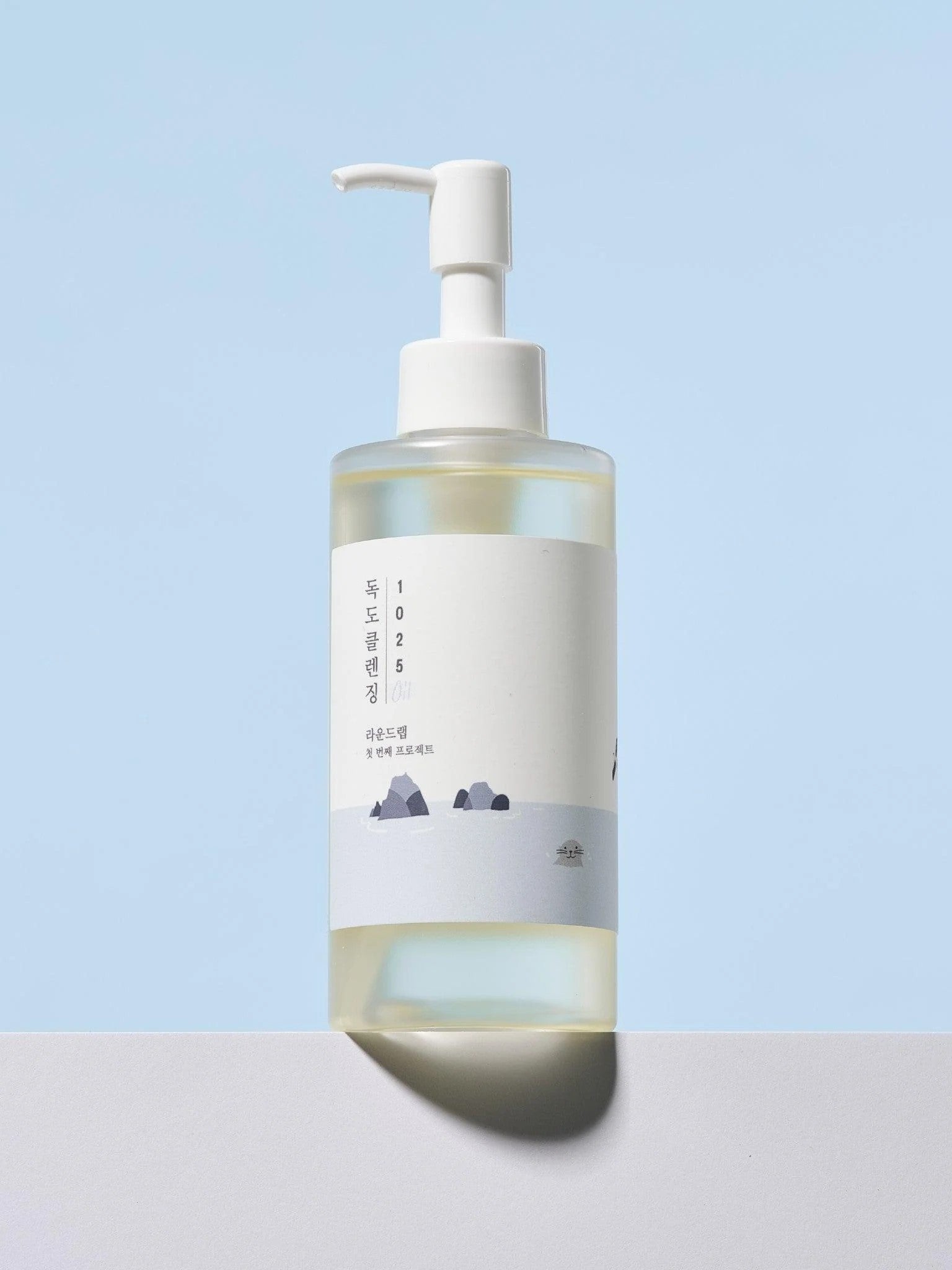 Round Lab 1025 Dokdo Cleansing Oil with a minimalist design, displayed against a pastel blue background, featuring a mountain silhouette on the label.
