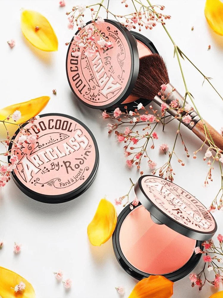 Too Cool for School Artclass By Rodin Blush in De Peche shade, surrounded by soft flowers and petals, with a makeup brush for effortless peach-toned application.