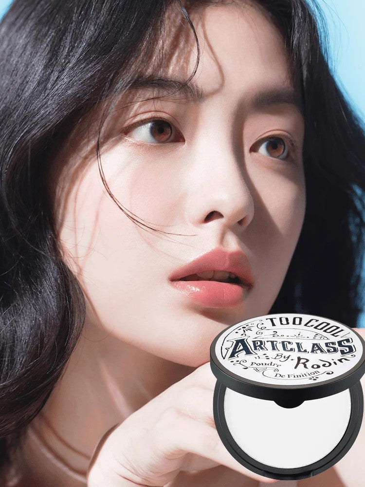 A model showcasing smooth, oil-free skin after applying Too Cool for School Artclass By Rodin Finish Setting Pact, with the product's elegant packaging details visible against a softly blurred background.