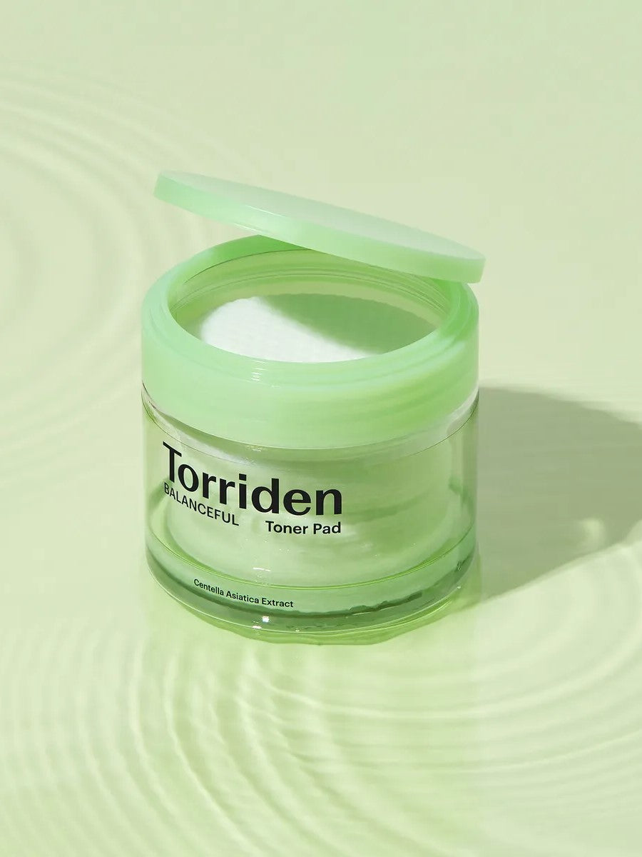 Transparent jar of Torriden Balanceful Toner Pad with a green lid, placed on a soft green rippled surface, showcasing its fresh and minimalist aesthetic.