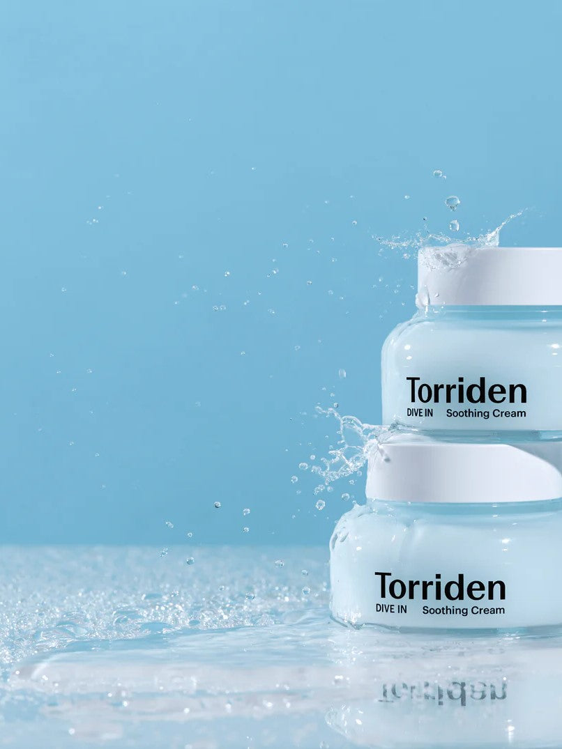 Two jars of Torriden Dive In Soothing Cream on a reflective surface, splashed with droplets against a soft blue background.