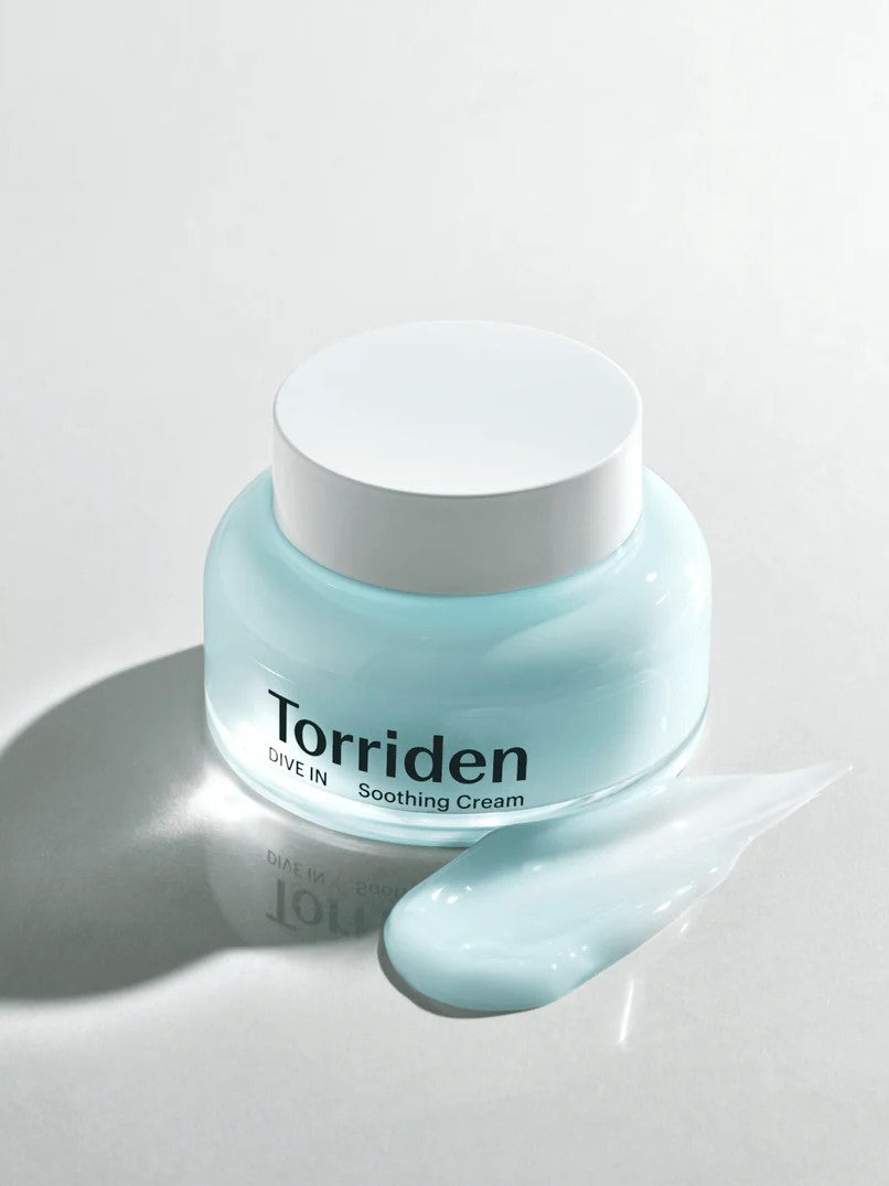 Jar of Torriden Dive In Low Molecular Hyaluronic Acid Soothing Cream in light blue, with a matching cream swatch beside it on a reflective surface.