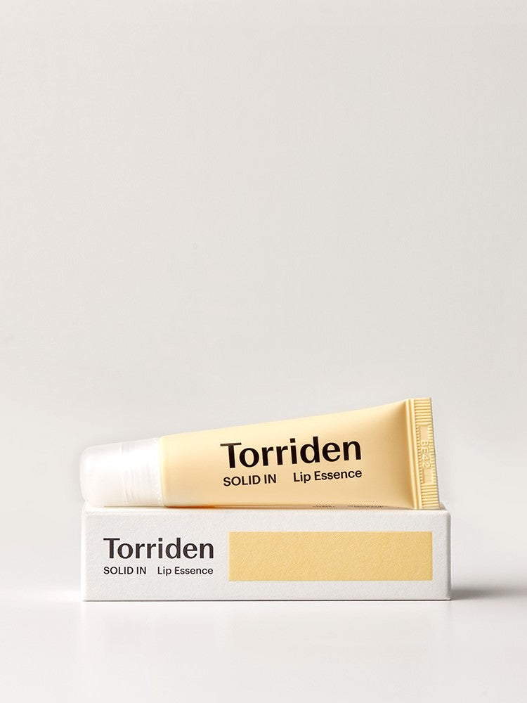 A tube of Torriden Solid In Lip Essence is placed atop its white box, showcasing minimalistic design with a yellow color scheme.