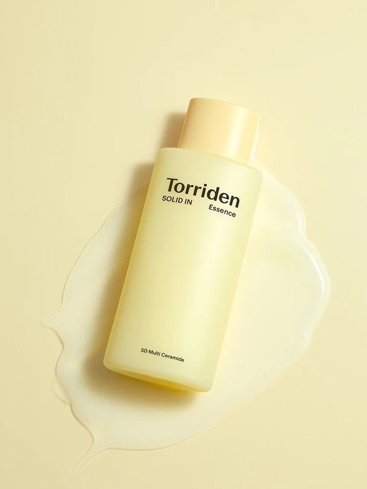 A bottle of Torriden Solid IN Essence with a pale yellow label sitting atop its creamy yet lightweight essence pool against a soft yellow background.