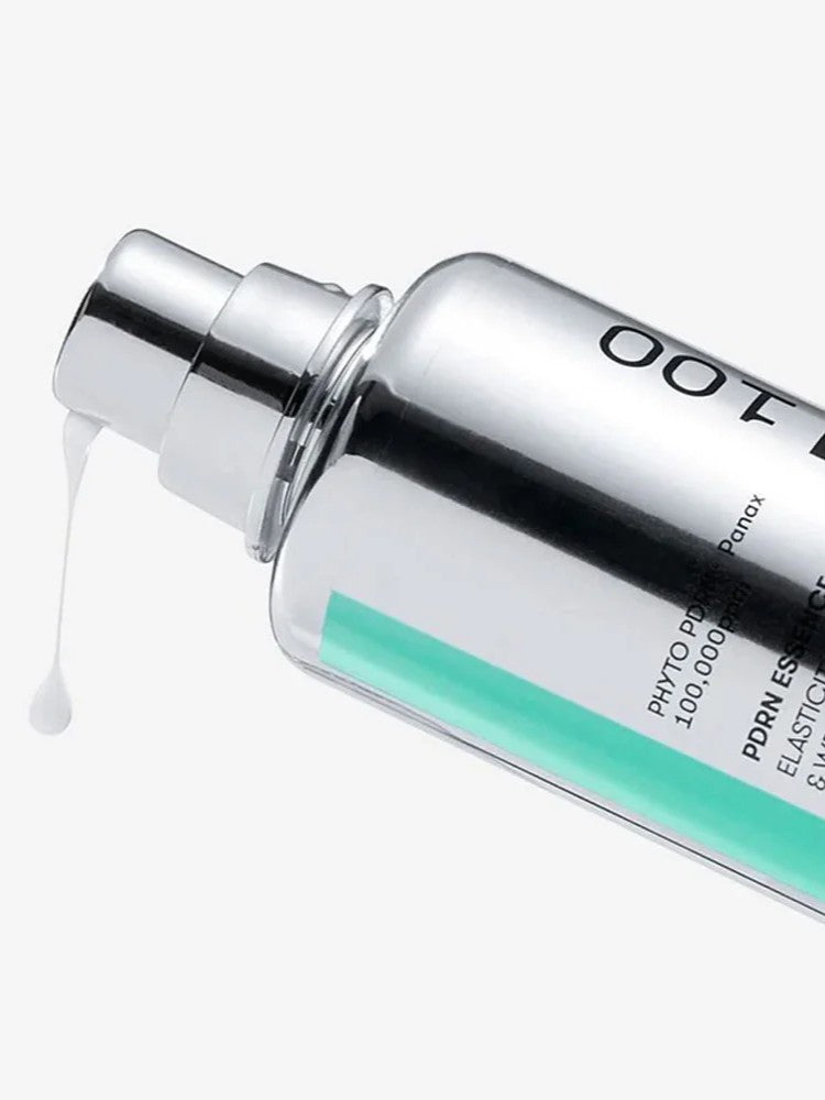 Close-up of a sleek silver bottle of VT Cosmetics PDRN Essence 100 with a pump, revealing its creamy white texture.
