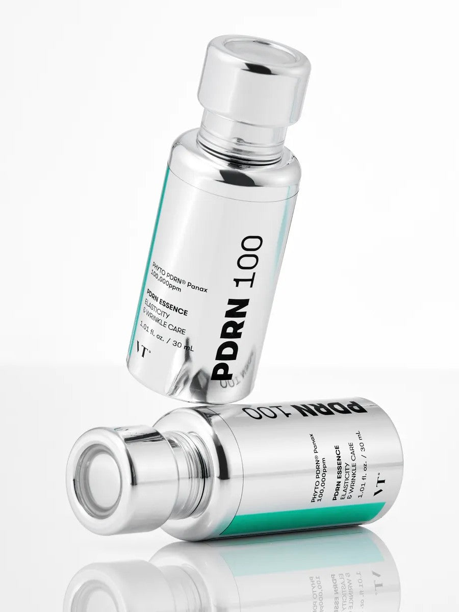 Two silver bottles of VT Cosmetics PDRN Essence 100, designed for elasticity and wrinkle care, displayed on a reflective surface.