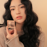 Model wearing a cozy beige sweater holding 3CE Mini Multi Eye Color Palette in Shade Flat Call, demonstrating its application and wearable look.