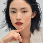 Model with shoulder-length wavy hair wearing 3CE Velvet Lip Tint in Shade Definition, showcasing bold pigmentation and a velvety matte finish.