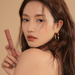 Model wearing gold hoop earrings against a muted beige background displaying 3CE Velvet Lip Tint in Shade Walk N Talk, highlighting the product’s creamy texture and bold pigmentation.