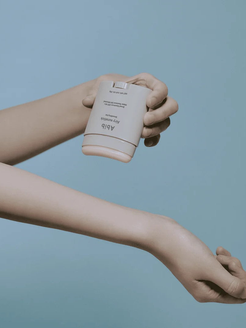 A hand holding the Abib Airy Sunstick over an outstretched arm, showcased against a light blue background, emphasizing its portable design and ease of application.