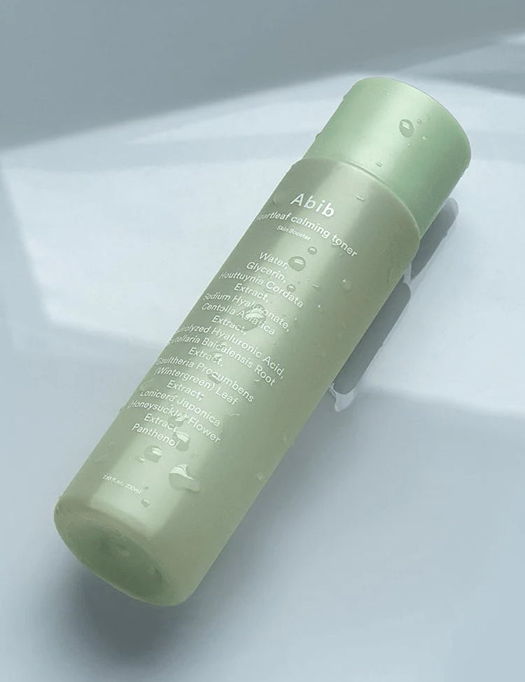 A green bottle of Abib Heartleaf Calming Toner with water droplets, showcasing its calming and hydrating properties.