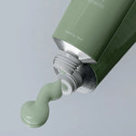 The Heartleaf Crème Calming Tube by a0d026 dispenses light green cream enriched with hyaluronic acid from its green tube. White text, partially visible on the tube, lists ingredients as the cap is removed. The background features a subtle, neutral light gray shade.