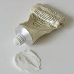 A squeezed tube of the Abib Jericho Rose Crème with a silver cap, placed beside a dollop of white cream on a light surface, showing the product texture.