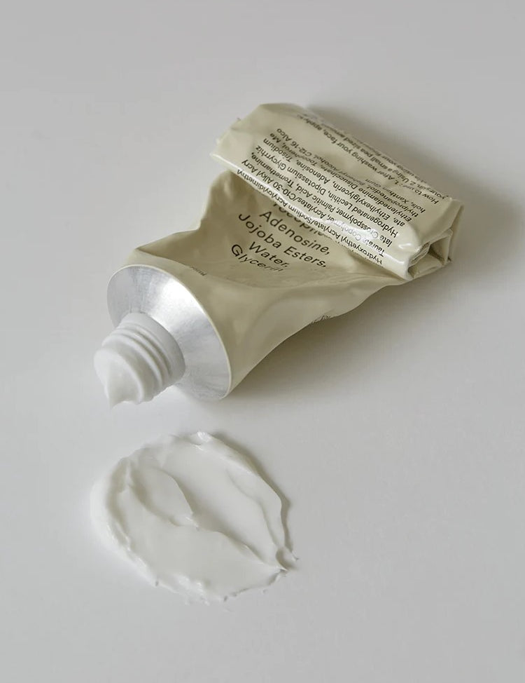 A squeezed tube of the Abib Jericho Rose Crème with a silver cap, placed beside a dollop of white cream on a light surface, showing the product texture.